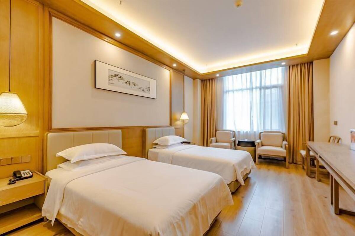 A hotel room with two beds, a desk, chairs, a lamp, and a framed picture on the wall.