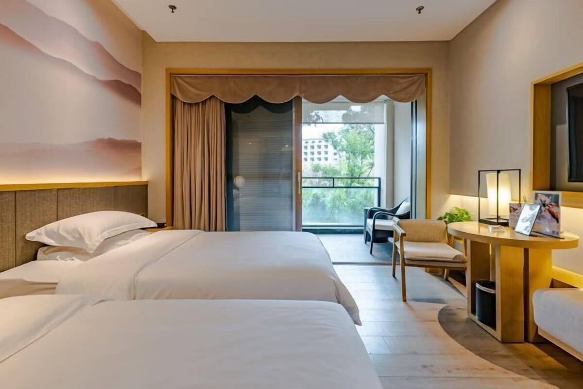 A hotel room with two beds, a desk, a chair, a balcony with a view, and a large window.