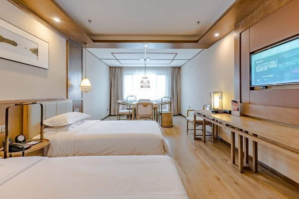 A hotel room with two beds, a desk, a chair, a TV, and a window with curtains.