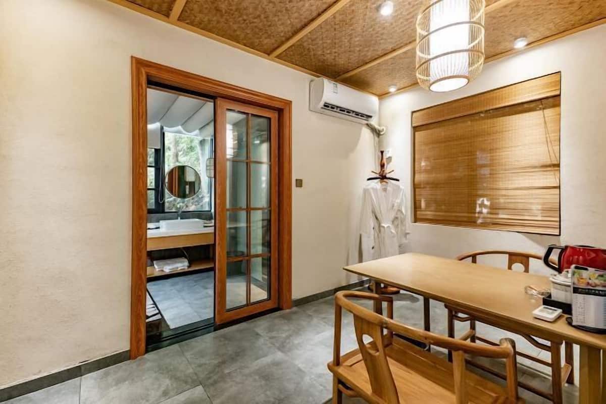 A room with a wooden dining table, chairs, a sliding glass door leading to a bathroom, and a ceiling fan.