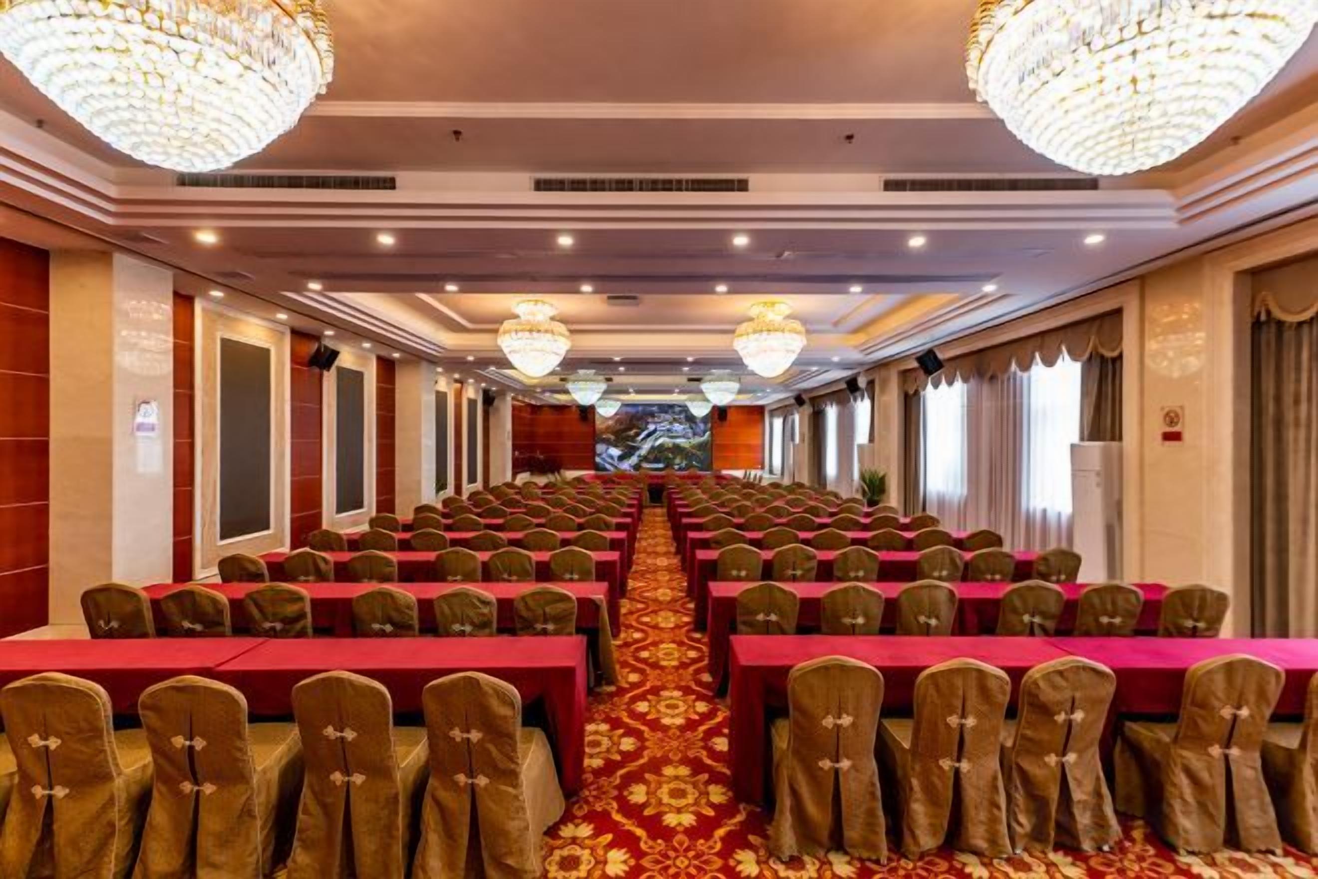 Un salón de banquetes con filas de mesas y sillas, candelabros y piso alfombrado.