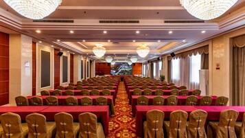 Un salón de banquetes con filas de mesas y sillas, candelabros y piso alfombrado.