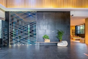 Un vestíbulo moderno con una pared de piedra oscura, un separador de madera con listones y un banco con plantas en macetas.