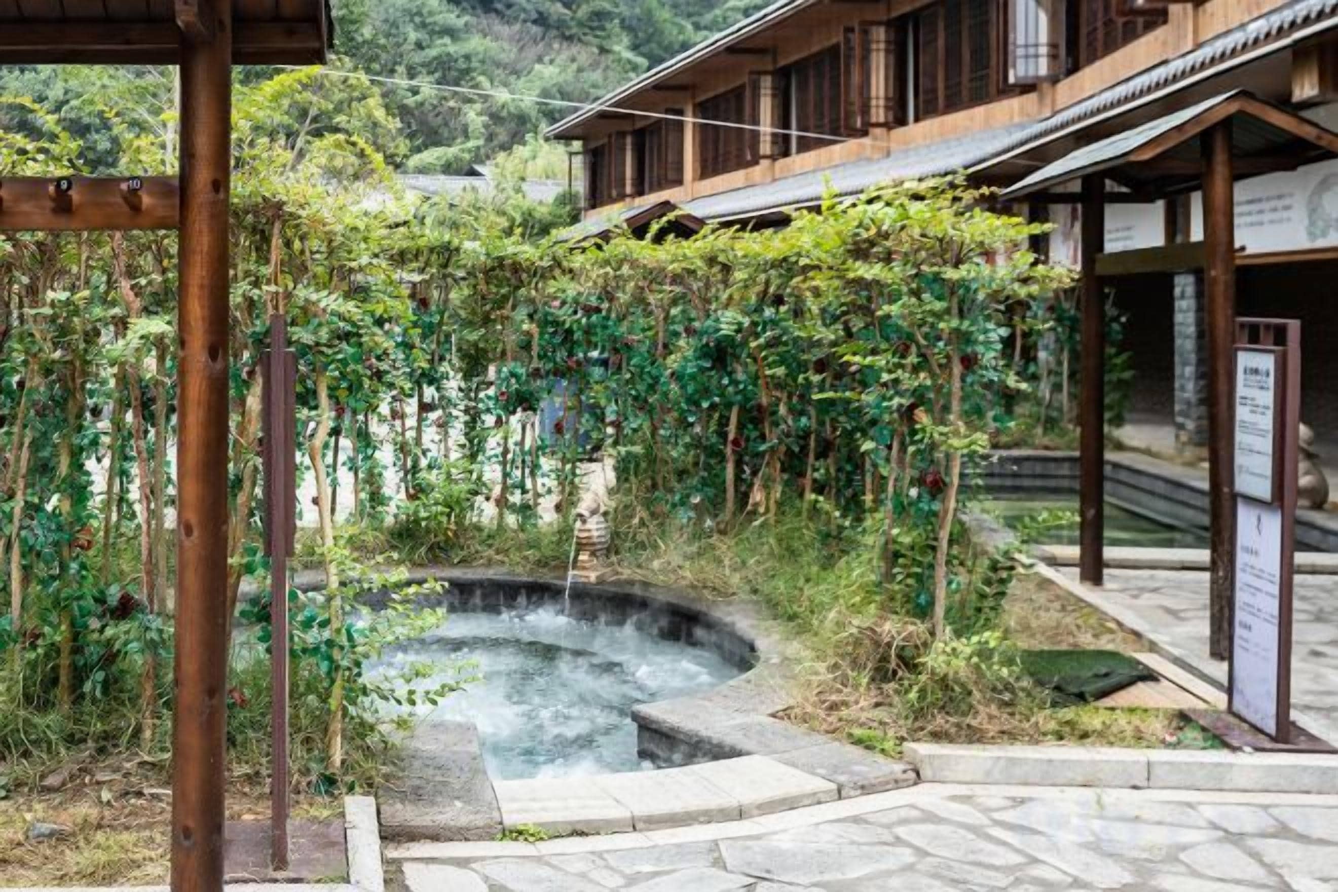 A traditional Japanese-style building with a hot spring, surrounded by lush greenery and a stone pathway.