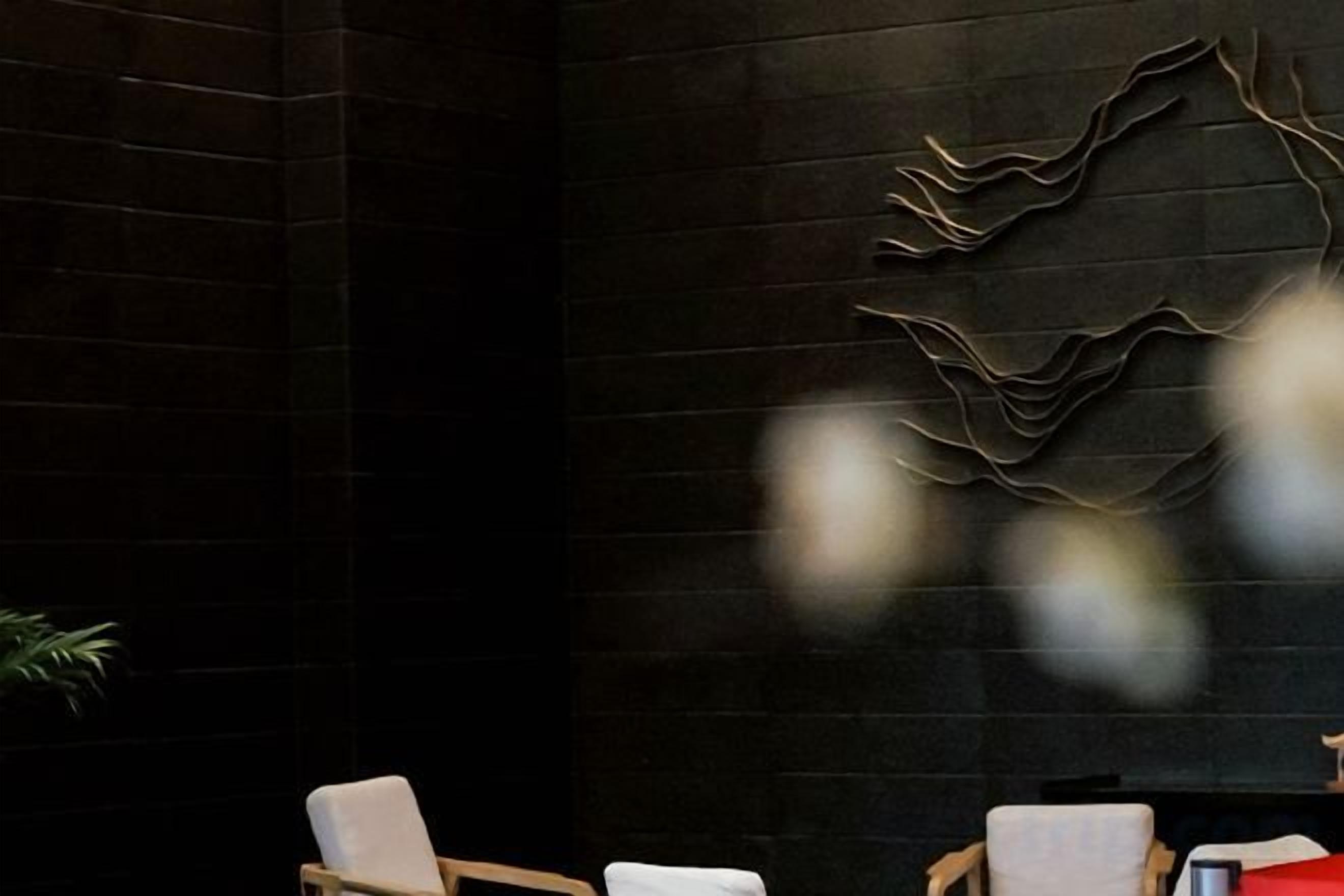 A reception area with a dark brick wall, a modern abstract wall art piece, and two chairs with white cushions.