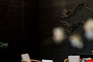Un área de recepción con pared de ladrillo oscuro, una obra de arte abstracta moderna y dos sillones con cojines blancos.