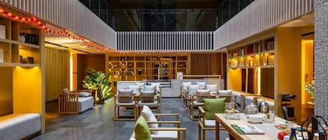 A spacious indoor area with a high ceiling, seating arrangements, and a central table with items on it.