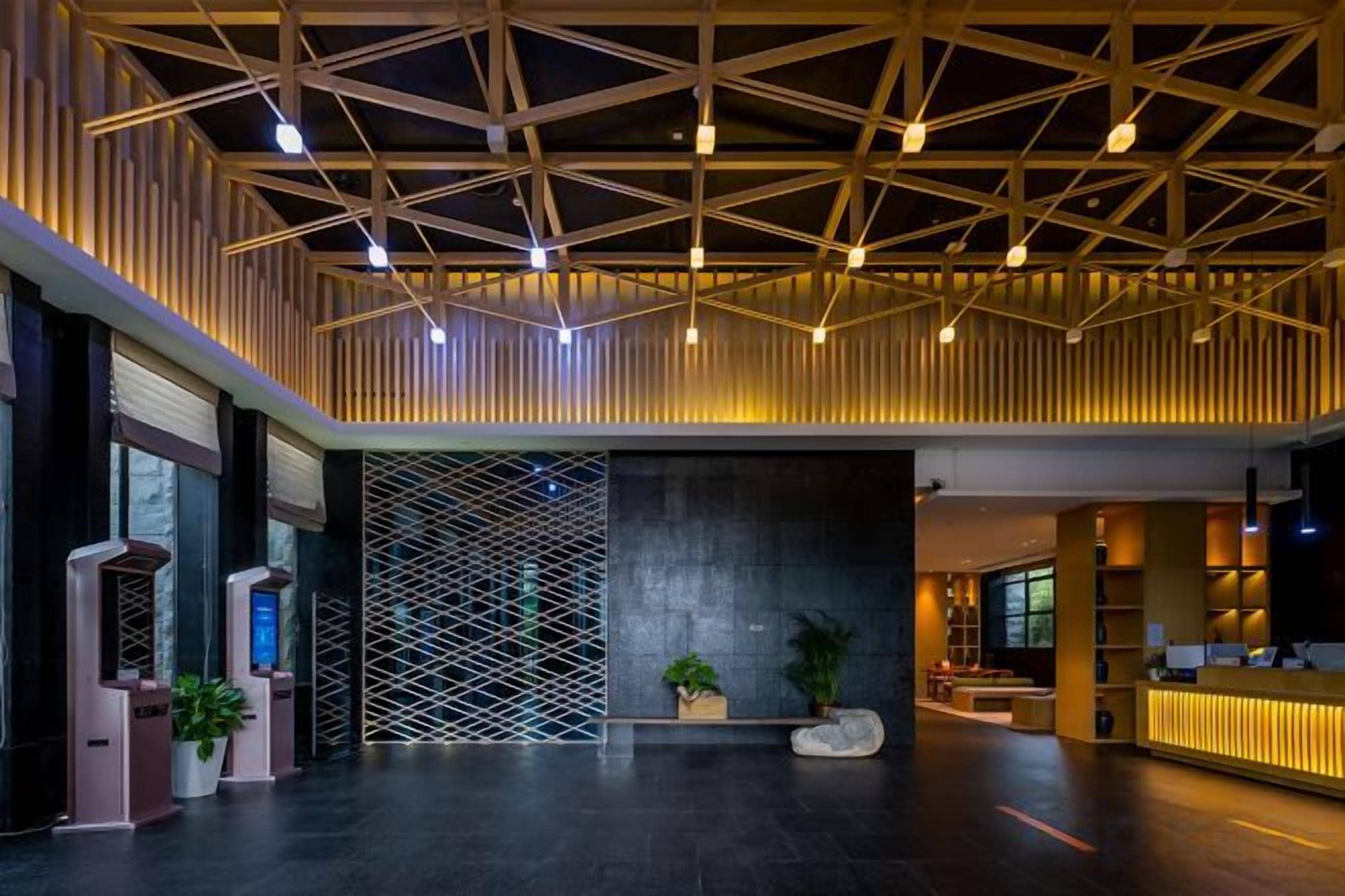 En moderne lobby med et geometrisk loftsdesign, en receptionsdisk og et siddeområde med planter.