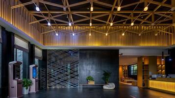 En moderne lobby med et geometrisk loftsdesign, en receptionsdisk og et siddeområde med planter.