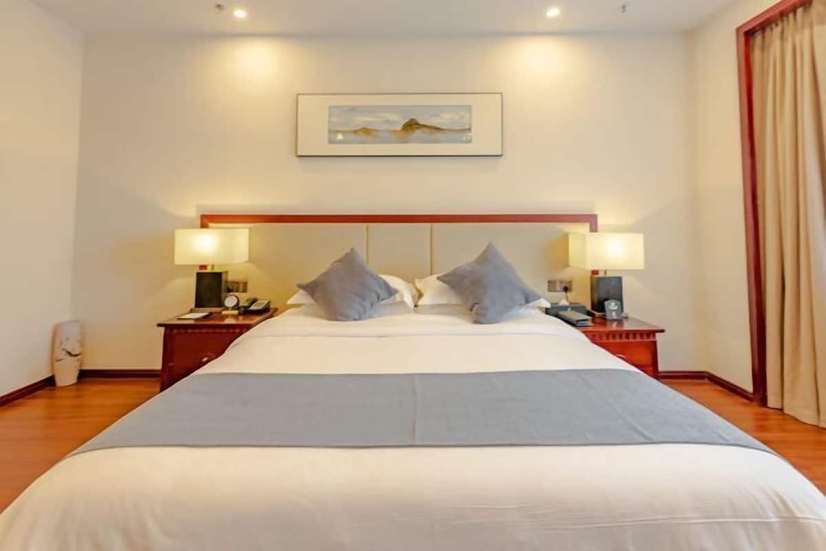A hotel room with a large bed, two bedside tables with lamps, a framed picture on the wall, and a curtain on the window.
