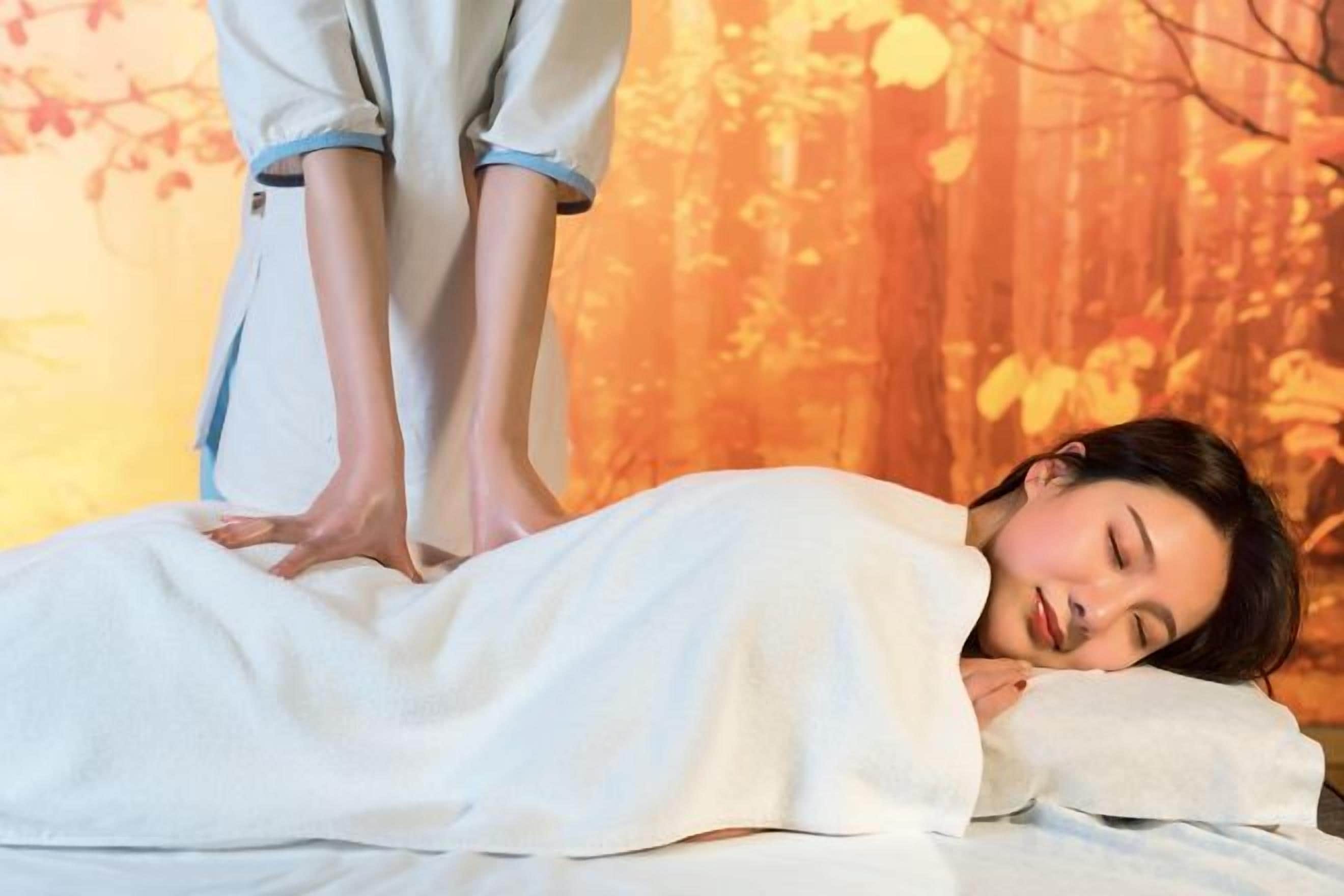 A person lying on a bed receiving a foot massage.