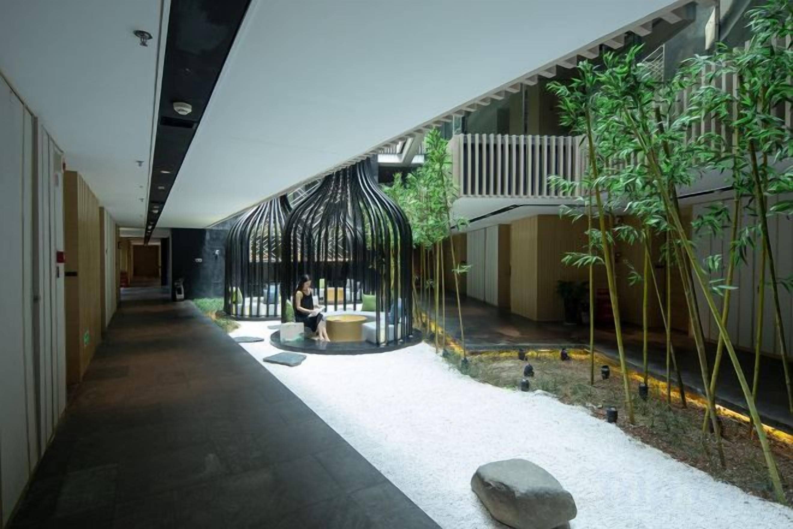 Un pasillo con una zona de estar, un pequeño elemento acuático y plantas de bambú.
