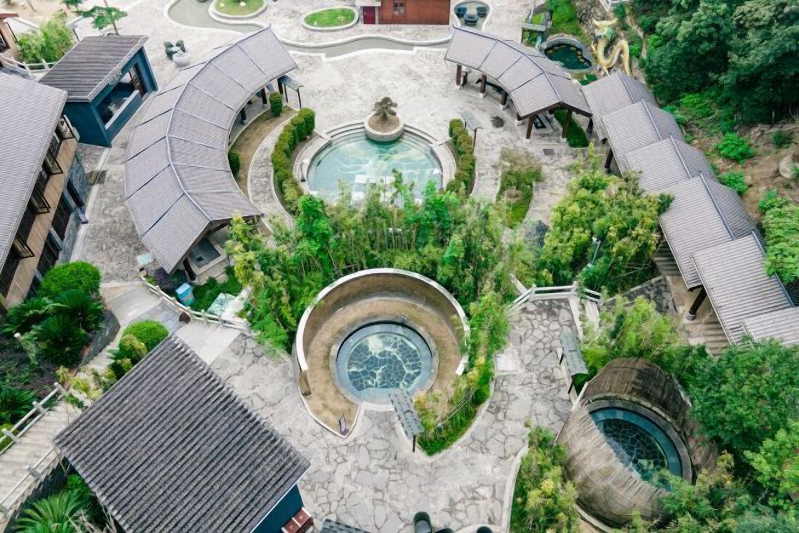 Vista aerea di un cortile con una fontana centrale, circondato da edifici dalle curve coperture e una piscina.