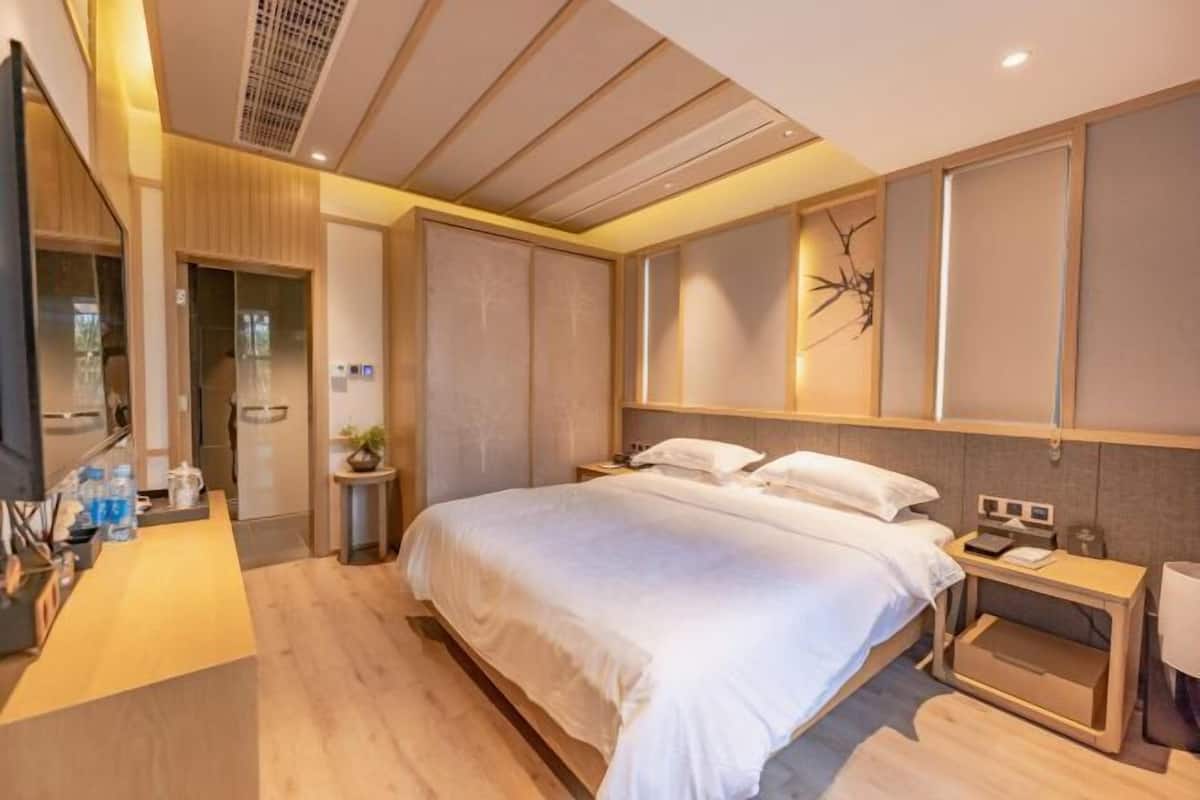 A modern hotel room with a large bed, bedside tables, a desk, and a mirror.