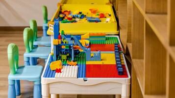 A table with a LEGO playset, blue chairs, and a wooden shelf.