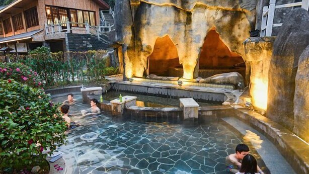 A hot spring area with stone-tiled pools and seating areas, surrounded by lush greenery and a rustic building in the background. - Tangtaizong Hot Spring Resort (Lushan City)