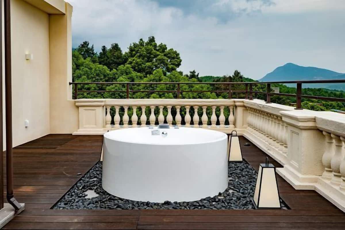 A circular hot tub on a balcony with a view of trees and a mountain.