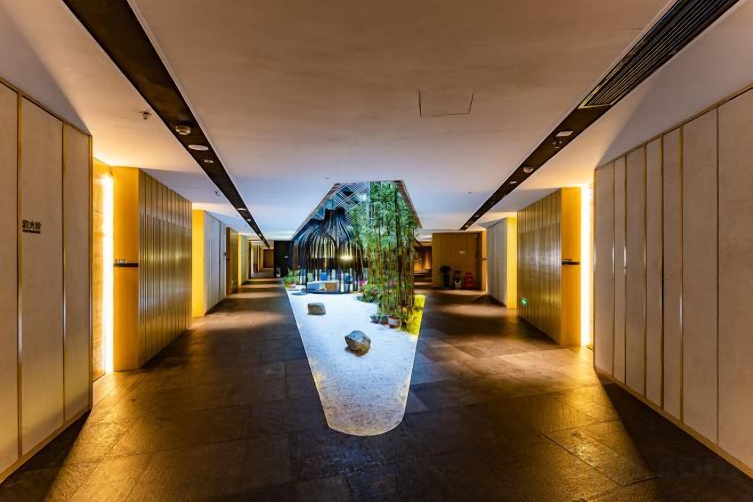 Un couloir d’hôtel avec un jardin central, un revêtement de sol en bois et un design moderne.