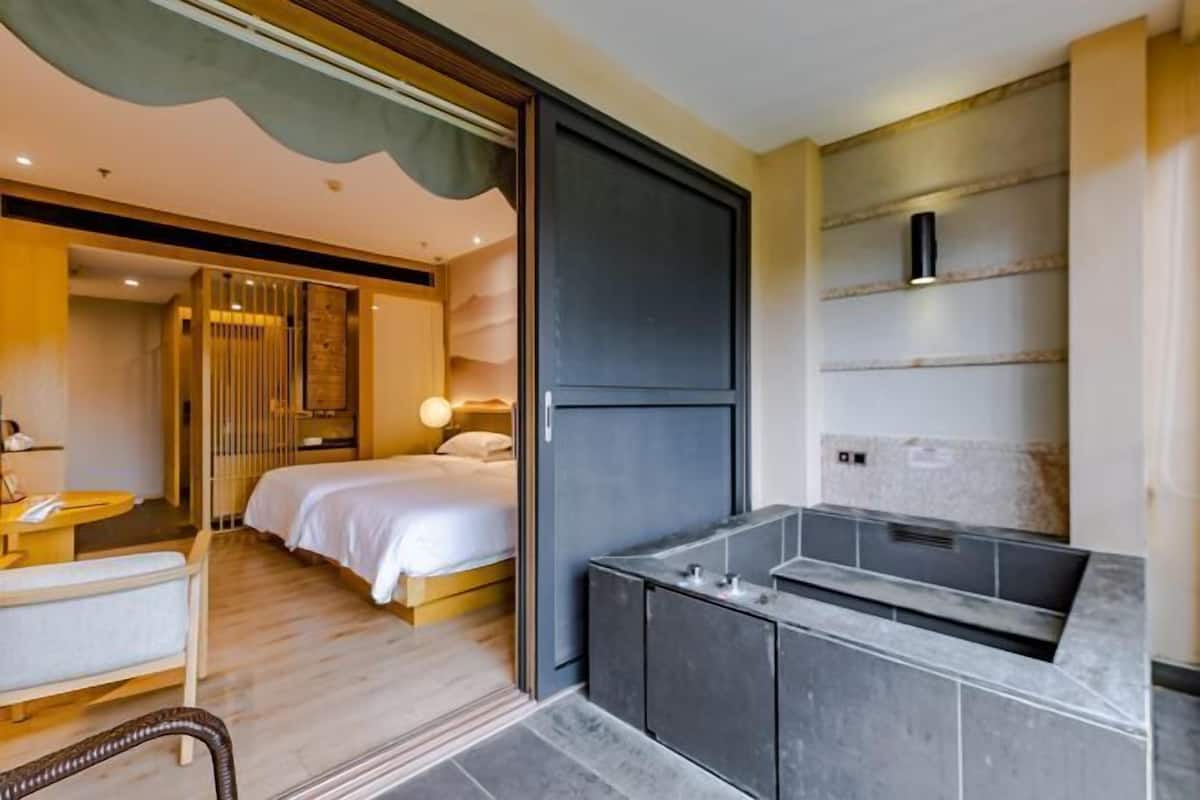 A modern hotel room with a bed, a sitting area, a bathroom with a bathtub, and a large mirror.