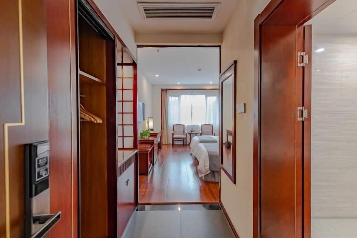 A hotel hallway leading to a room with a bed, a desk, and a chair.