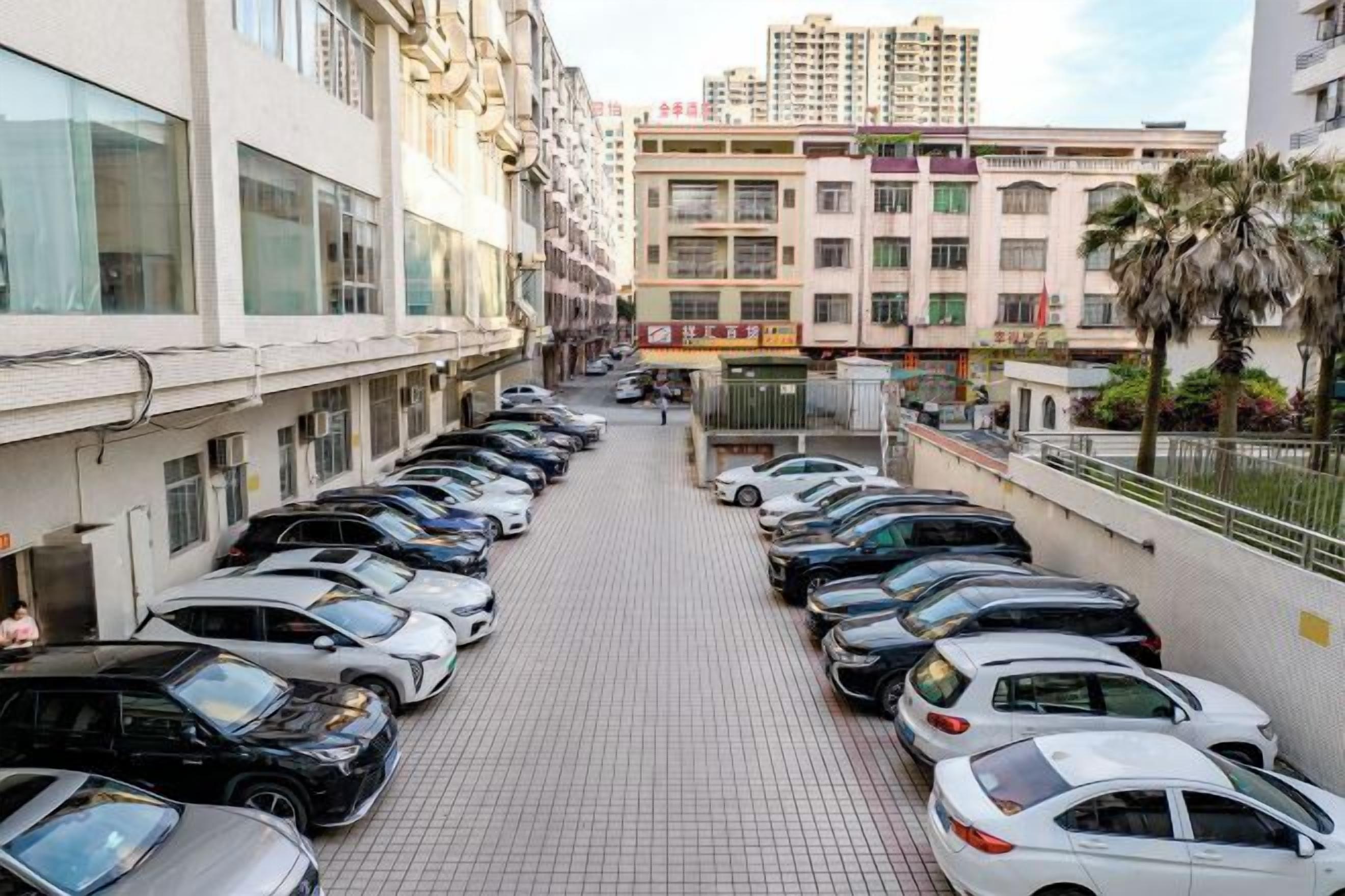 Un estacionamiento con varios coches aparcados en filas, junto a un edificio con un camino empedrado.