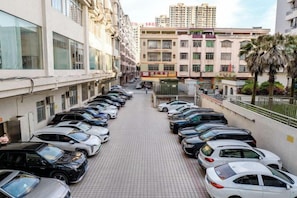 Un parking où de nombreuses voitures sont garées en rangées, à côté d’un bâtiment doté d’une allée piétonne carrelée.