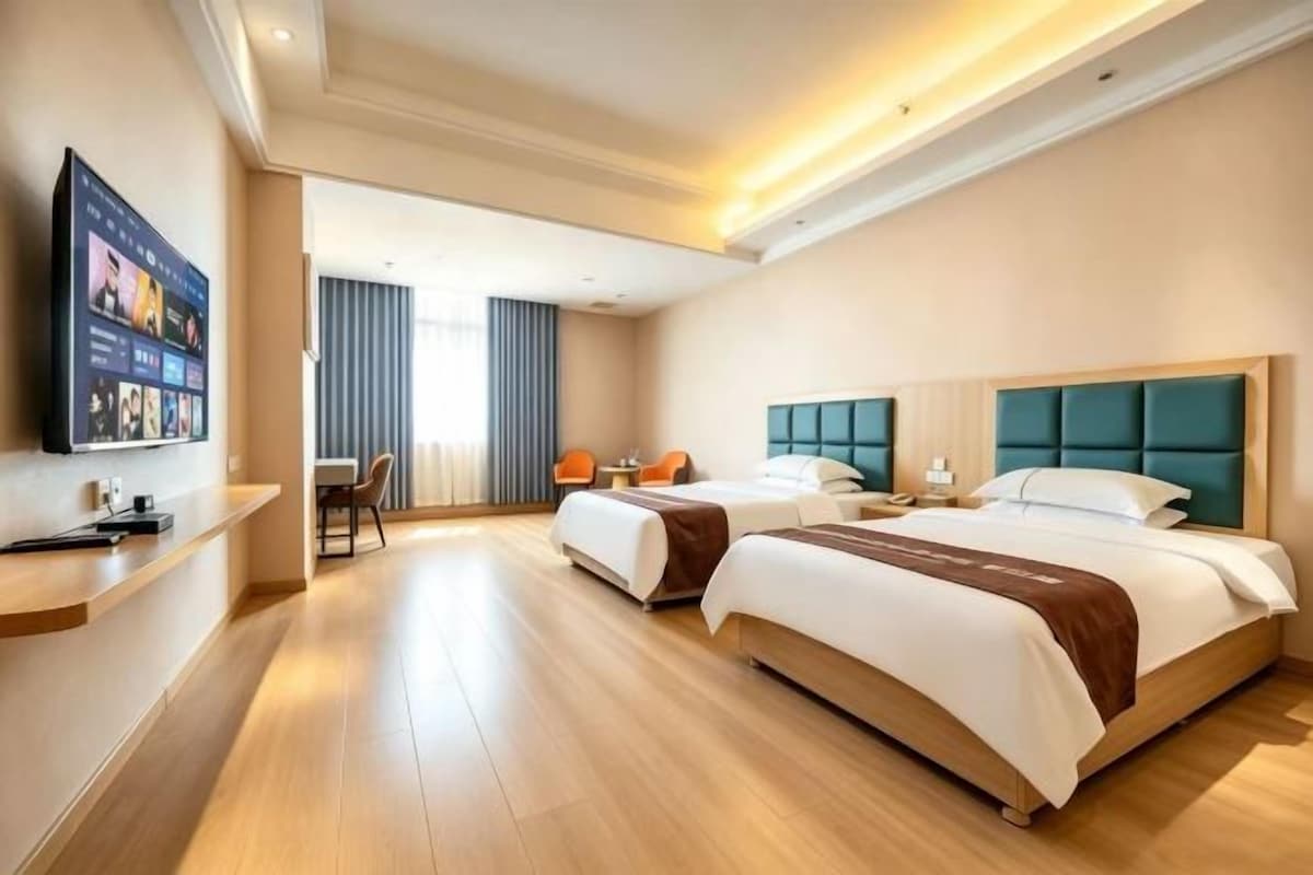 A hotel room with two beds, a desk, and a TV.