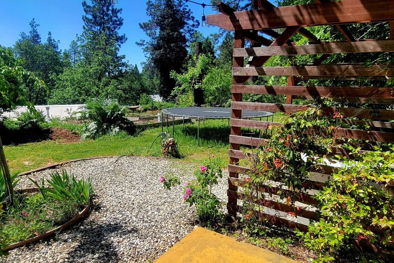 A garden with a wooden pergola, a trampoline, and a gravel path.
