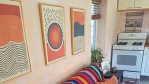 Ett vardagsrum med en färgglad, randig soffa, ett köksområde med vita vitvaror och abstrakt konst på väggarna.