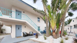 Un edificio de dos plantas con una escalera azul, una puerta con el número 4 y una zona de estar exterior con una palmera.