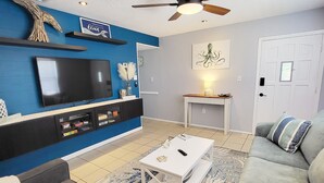 Una sala de estar con televisor de pantalla plana, ventilador de techo, sofá, mesa de centro y alfombra.