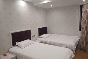 A hotel room with two beds, a nightstand, and a window with curtains.