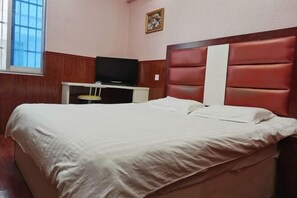 A bedroom with a bed, a television on a stand, and a window.