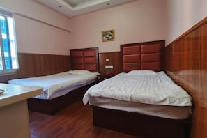 A room with two beds, wooden headboards, a small table, and a window.