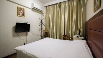A hotel room with a bed, a television, an air conditioning unit, a chair, and a desk with a lamp.