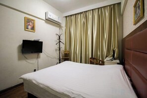 Habitación de hotel con cama, televisión, aire acondicionado, una silla y escritorio con lámpara.