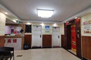Zona de recepción de un hotel con mostrador, un basurero, tres puertas y un cartel en la pared.