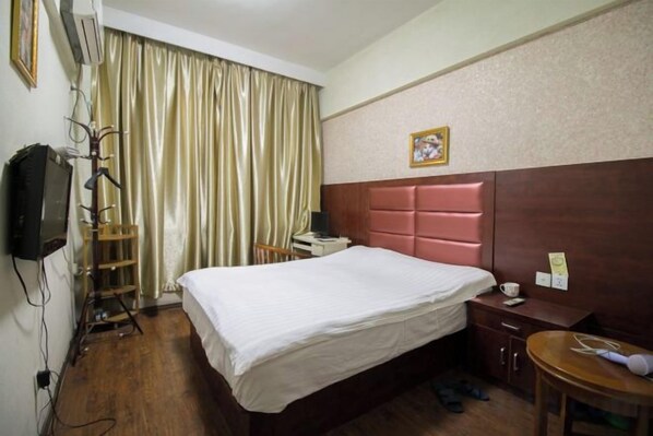 A hotel room with a bed, a desk, a chair, a television, and a curtain.