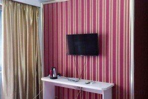 A room with a television mounted on a wall with striped wallpaper, a white console table with a kettle and a remote control, and a window with a curtain. - Jinhua Lianyi Hotel (Jinhua)