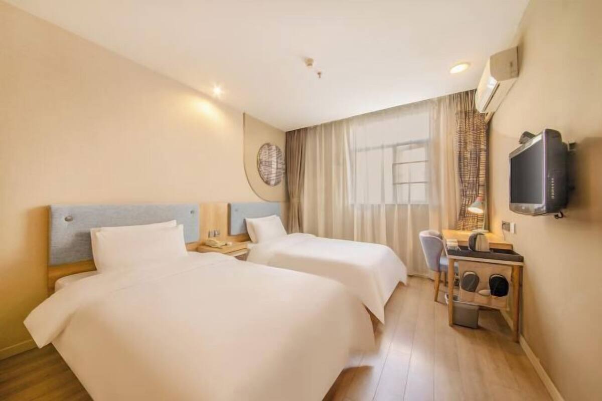 A hotel room with two beds, a desk, a chair, a television, and a window with curtains.