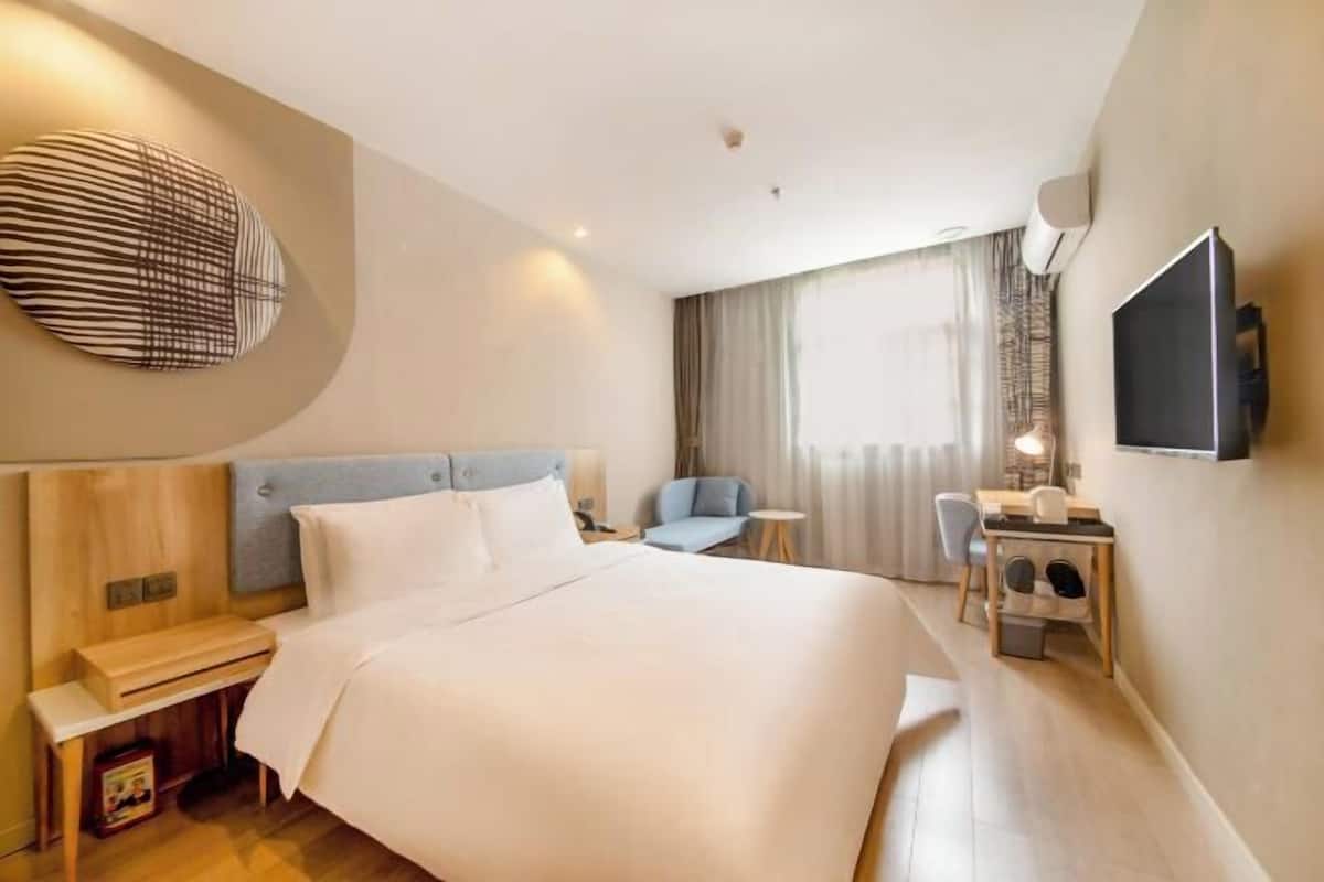 A hotel room with a large bed, a desk with a chair, a television, and a window with curtains.