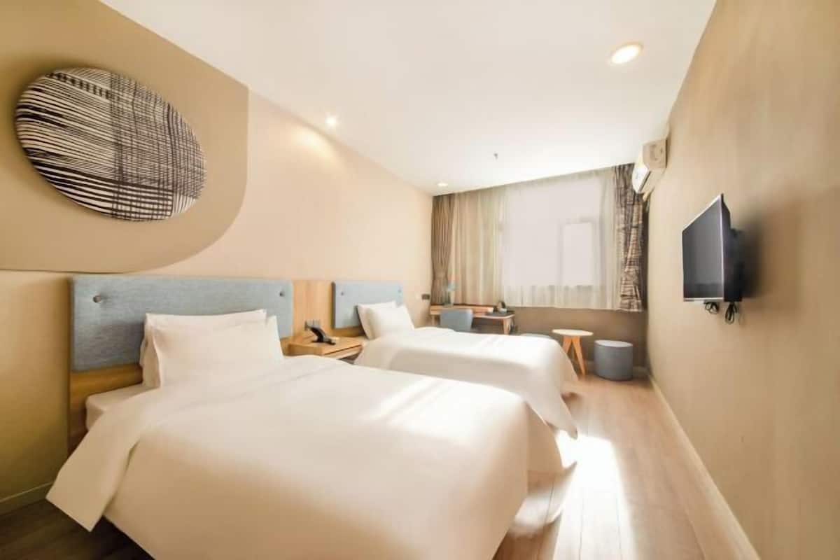 A hotel room with two beds, a TV, a desk, and a window with curtains.