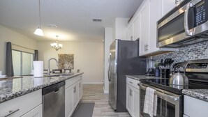 A modern kitchen with stainless steel appliances, white cabinets, and a granite countertop.