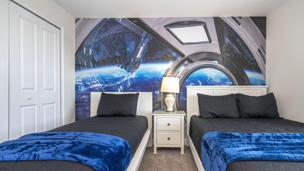A bedroom with two beds, a nightstand, and a wall mural of space.