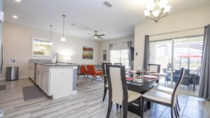 A spacious kitchen with a central island, dining area with chairs, and a large sliding glass door to the outdoors.