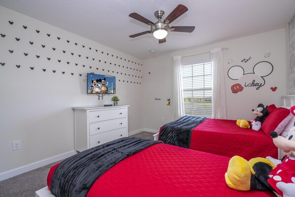 A bedroom with two beds, a ceiling fan, a window with blinds, and Mickey Mouse decorations. - 3157- Great Family Home near Disney, private pool, Storey Lake Resort. (Kissimmee)