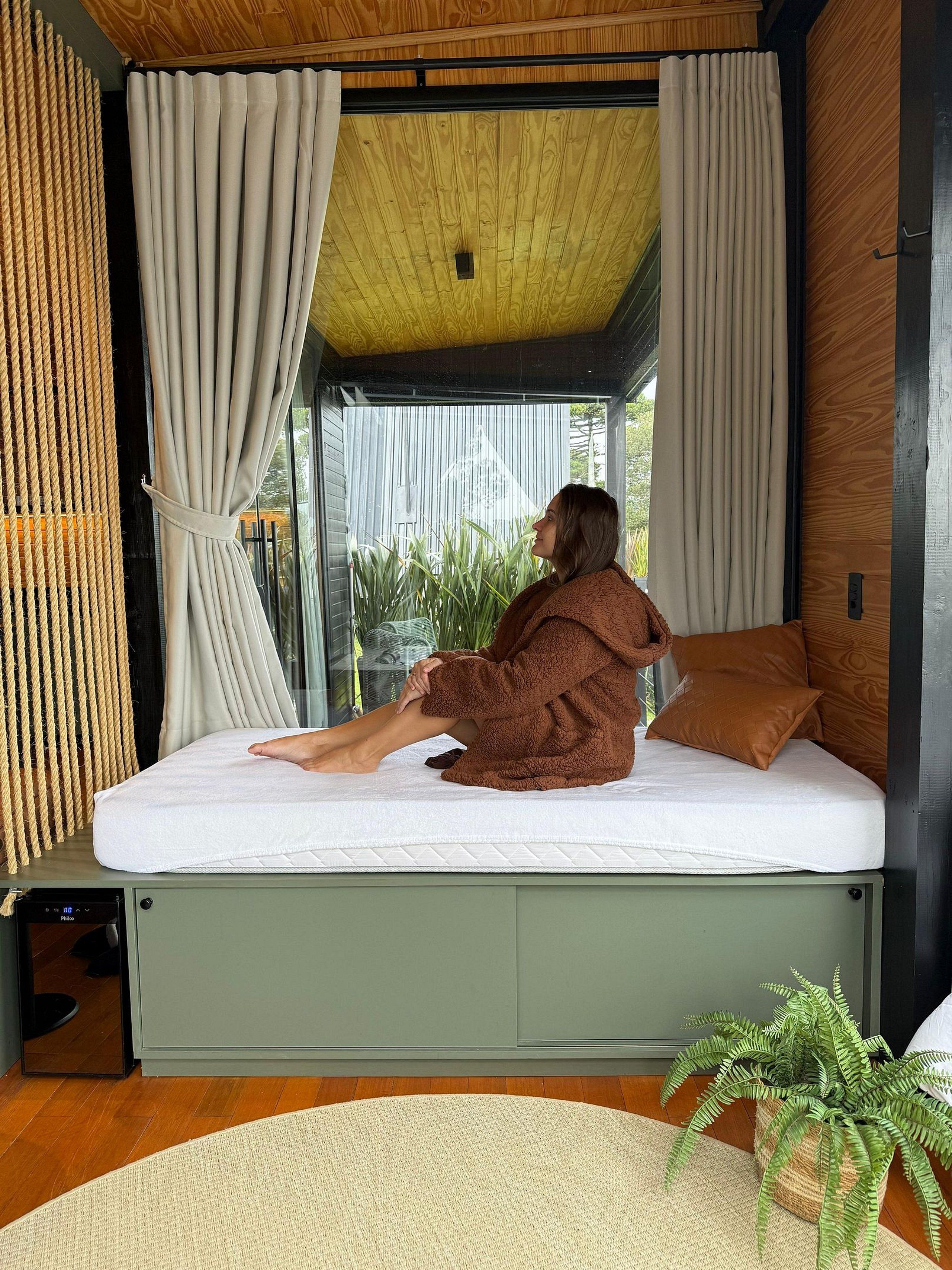 Un dormitorio moderno con cama empotrada, techo de madera y vistas amplias a través de grandes ventanales.
