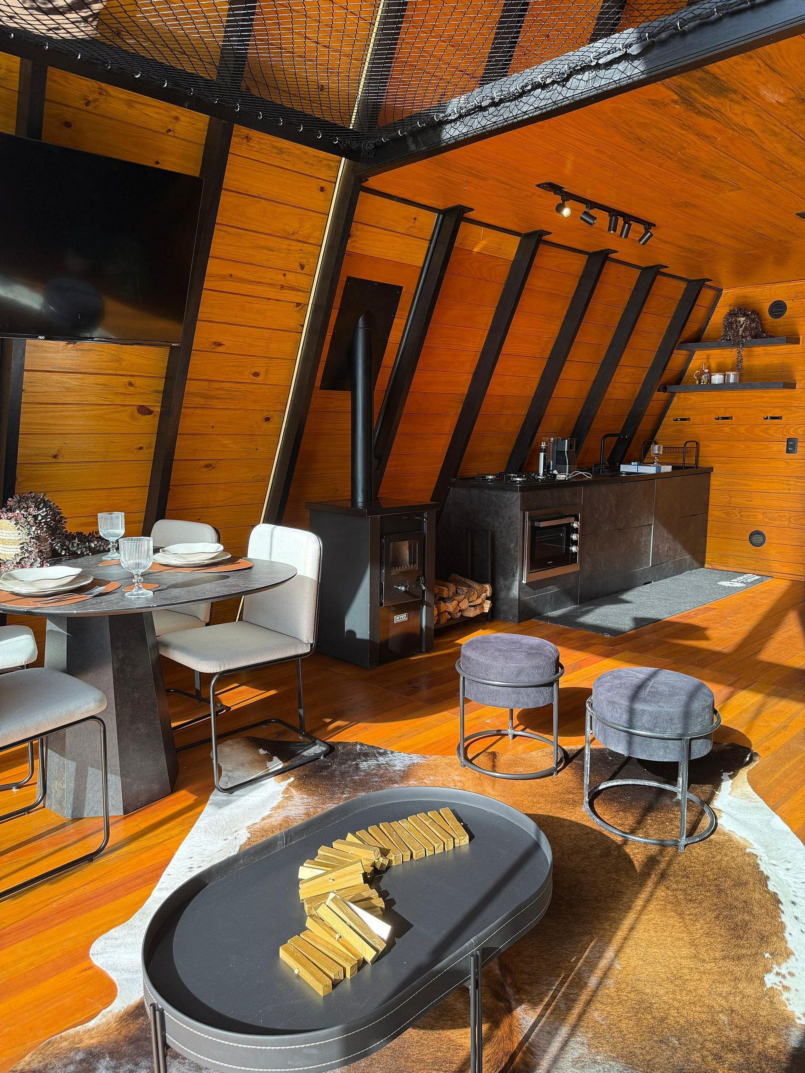 A cozy, rustic interior with a wooden ceiling, a fireplace, a dining area with chairs, and a table set for a meal.