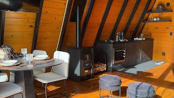 A cozy, rustic interior with a wooden ceiling, a fireplace, a dining area with chairs, and a table set for a meal.