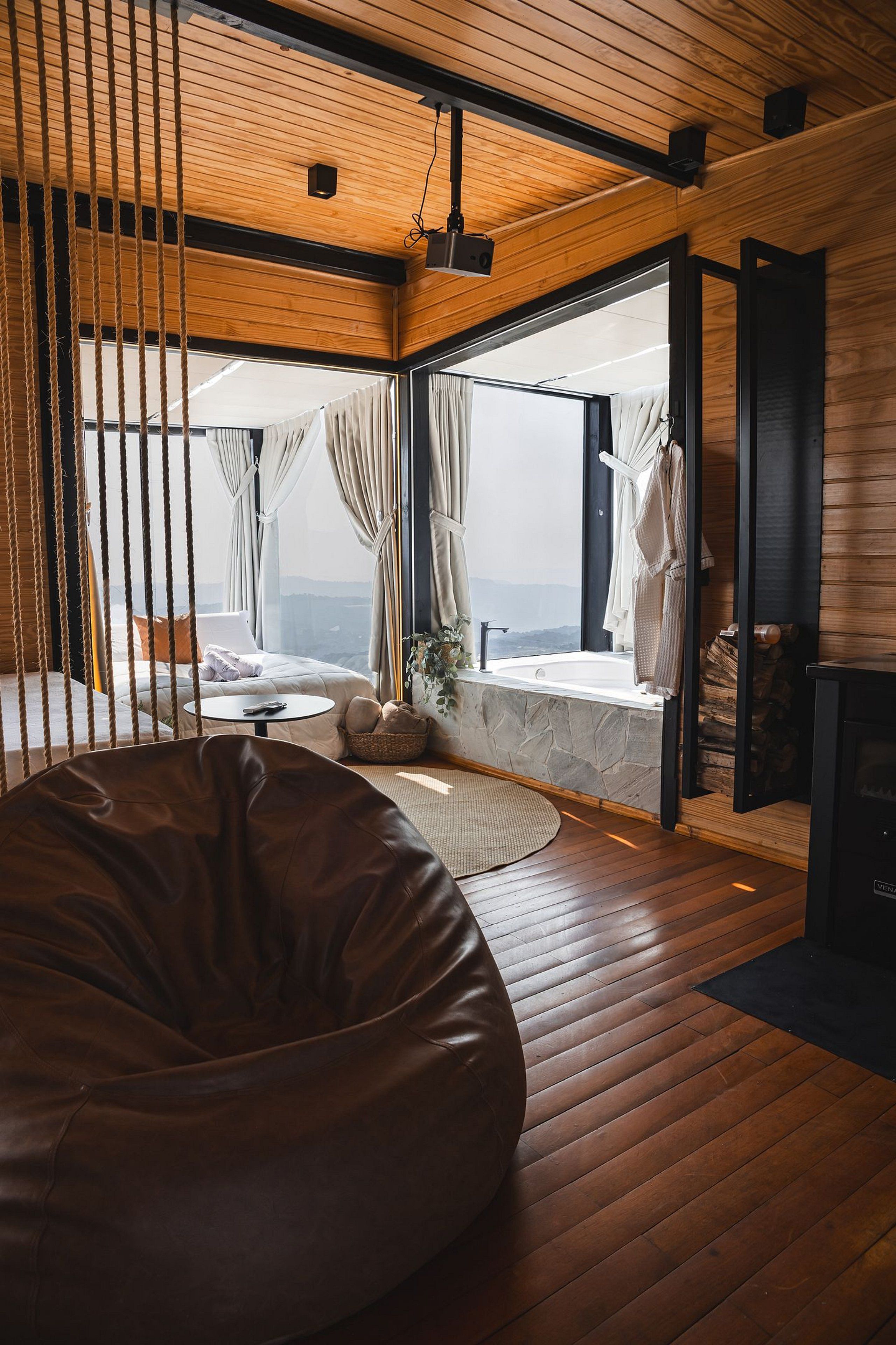 A modern room with a large window, a stone bathtub, a wooden floor, and a leather bean bag.